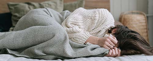 girl with dark hair lying on side with blanket pulled up to face