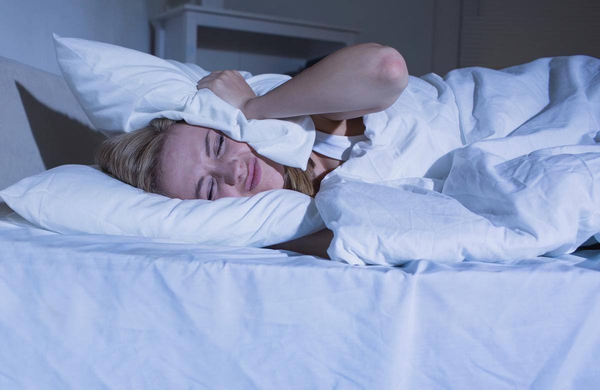 Photo of frustrated woman with pillow over one side of her head in bed -- a person sleeping with tinnitus.